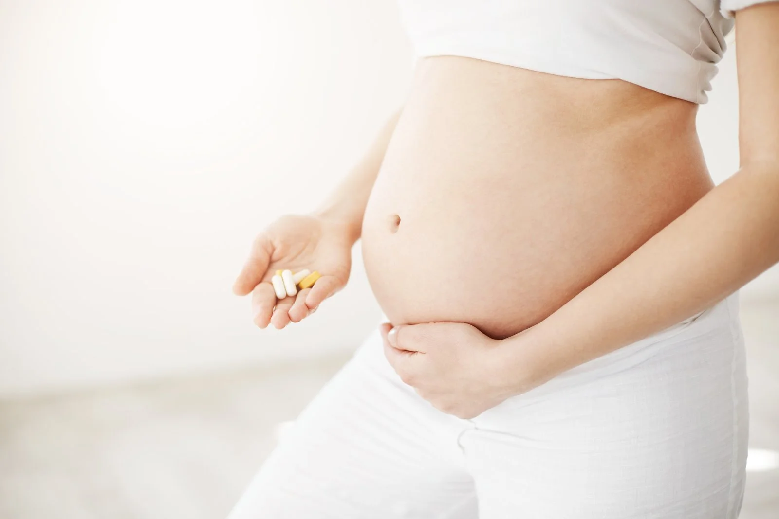 Pregnant woman holding folic acid and vitamin D supplements with a glass of water