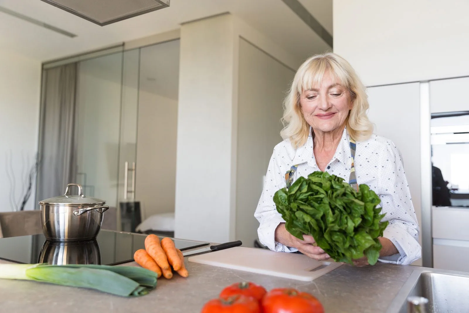 Smiling woman in her fifties preparing a fresh salad in her kitchen