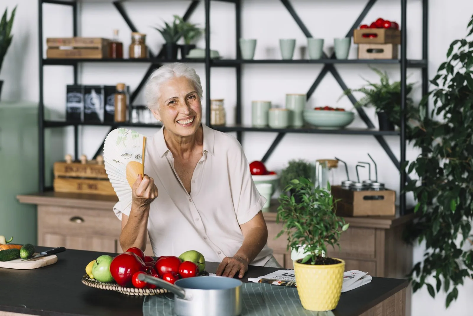 Woman sitting in her kitchen cooling herself with a fan during a hot flush